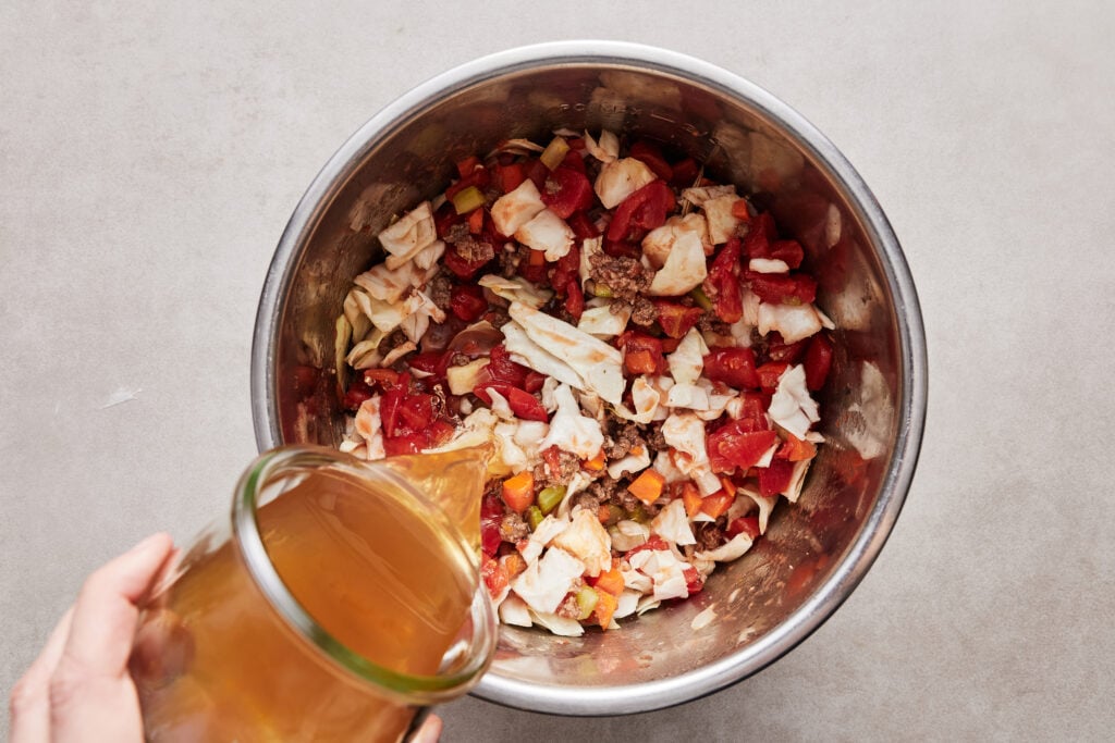 pouring broth on top of the veggies and beef before turning on the pressure cooker