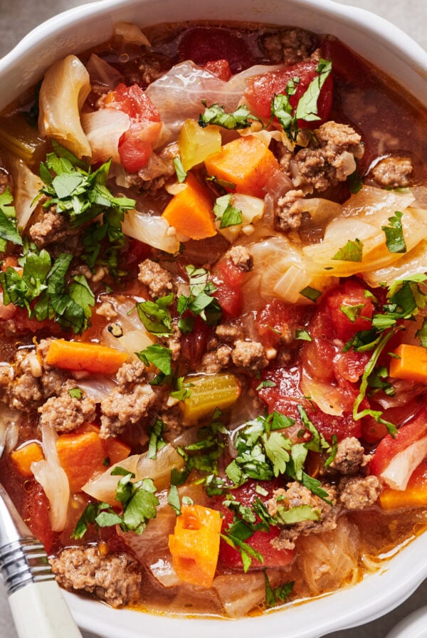 Instant pot cabbage soup in a white bowl with a spoon resting on the side.