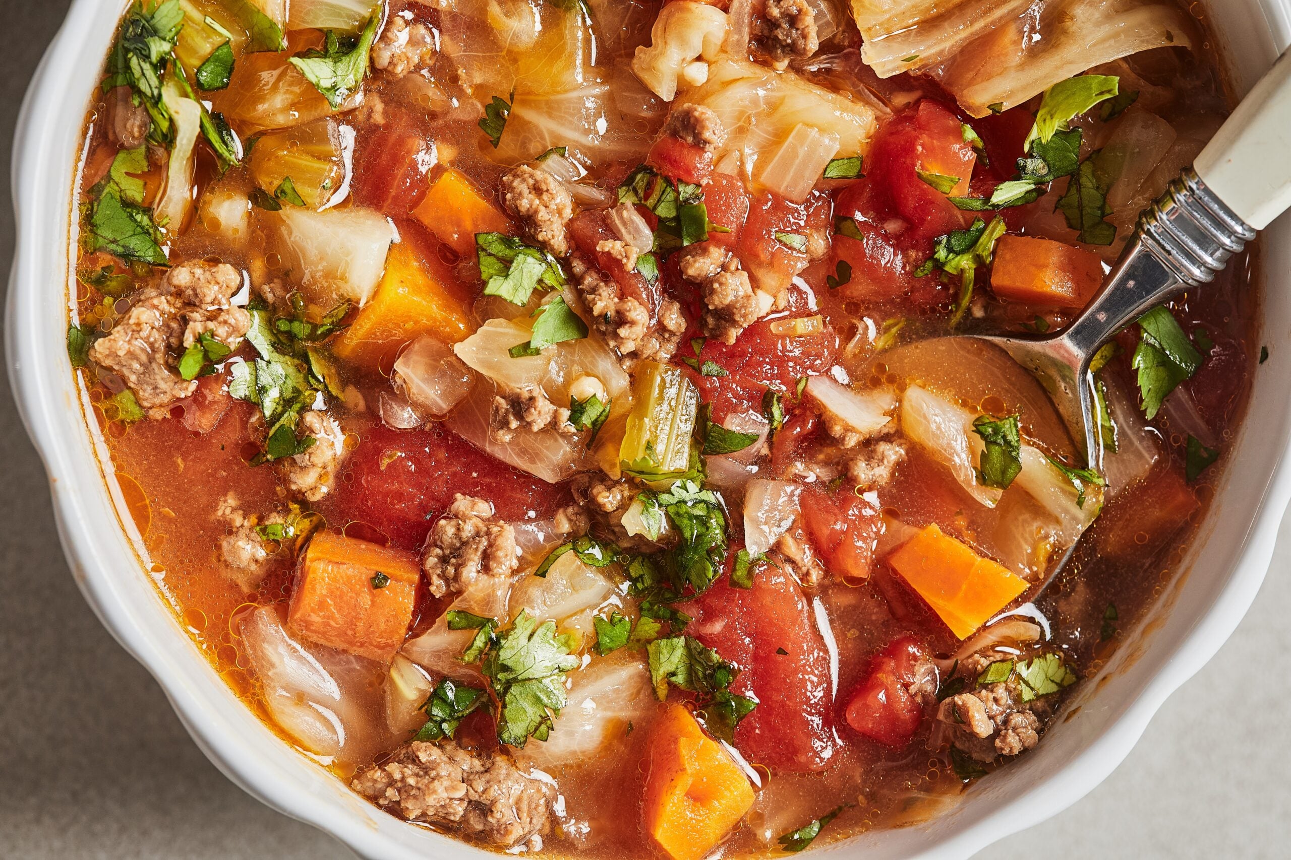 a close up photo of instant pot cabbage soup in a bowl with veggies, ground beef, and broth