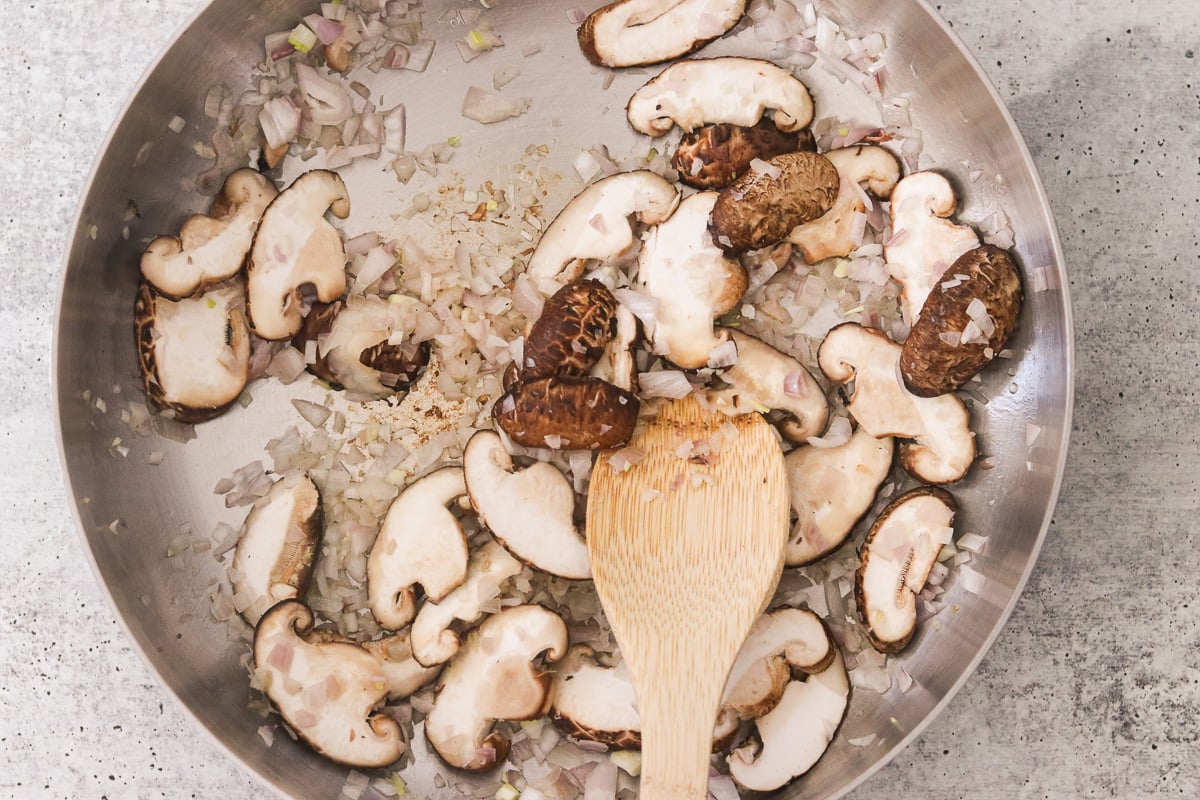 Shallots and sliced shiitake mushrooms sautéing in coconut oil in a large saucepan.