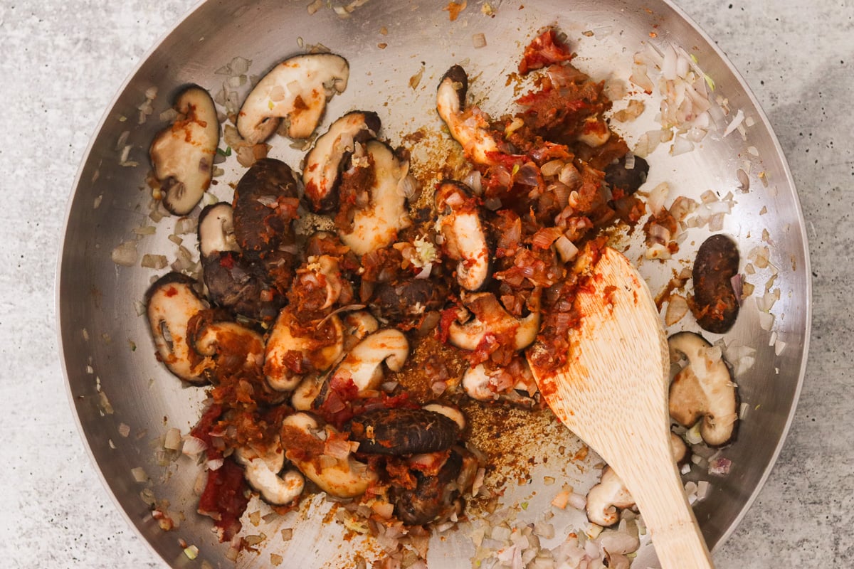 Garlic, ginger, red curry paste, and tomato paste cooking together in a saucepan.