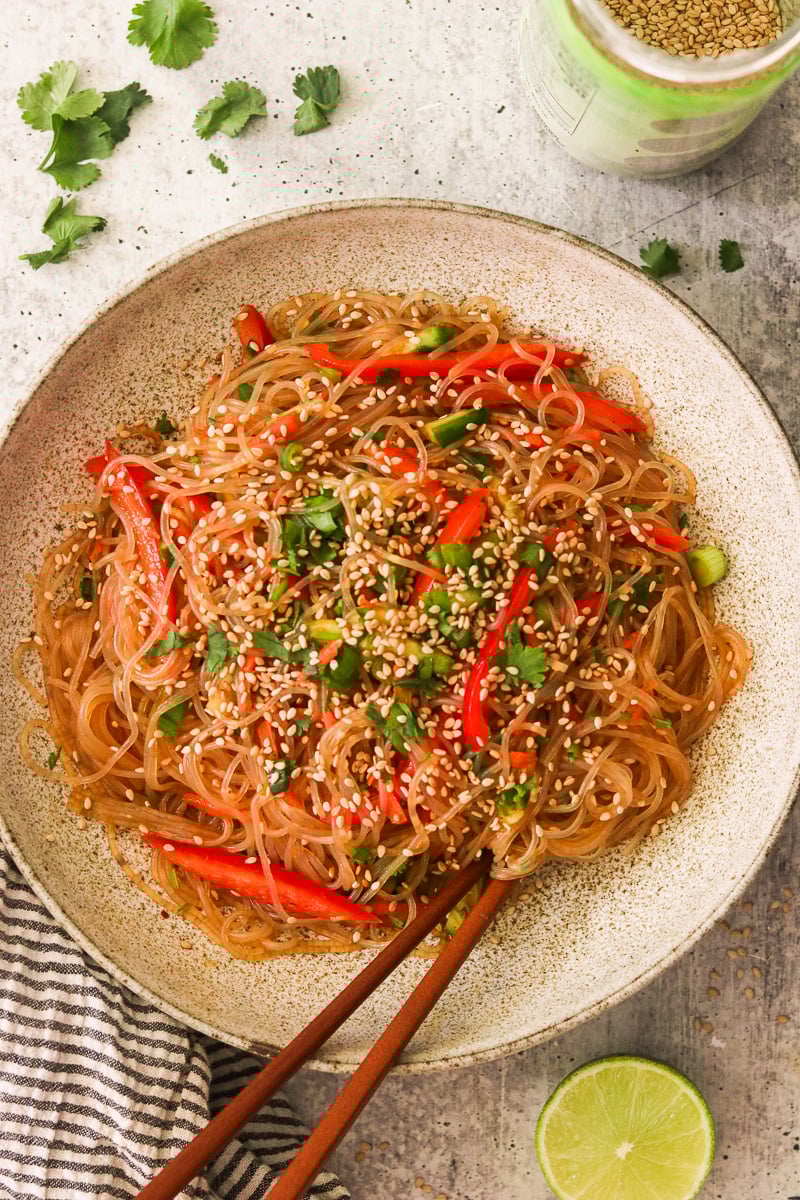Sesame noodle salad in a bowl garnished with fresh cilantro and sesame seeds, with chopsticks resting inside the bowl.