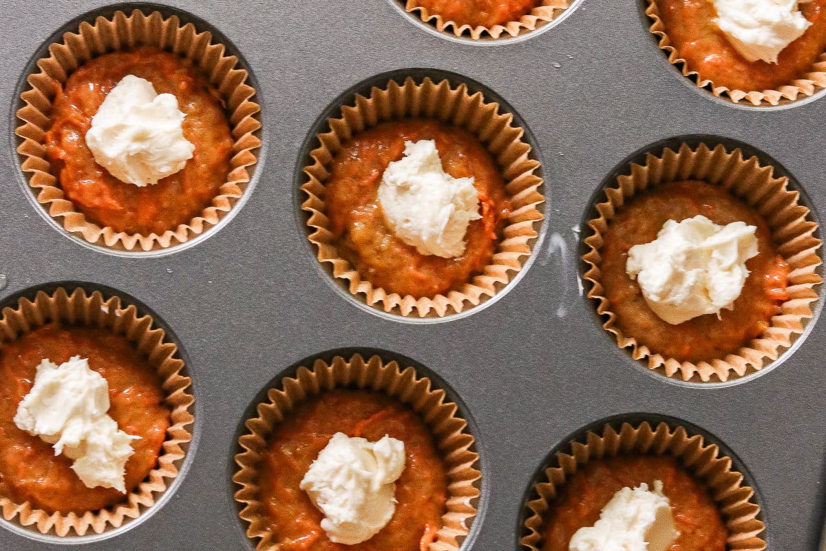 Muffin batter added to lined muffin cups with cream cheese filling placed in the center.