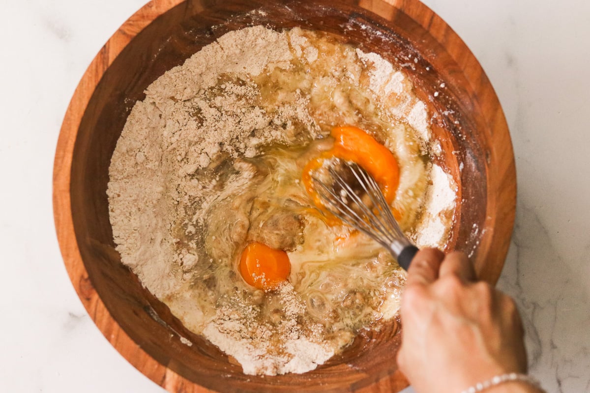 Wet ingredients—avocado oil, milk, eggs, and vanilla extract—added to the dry mixture in a wooden bowl.