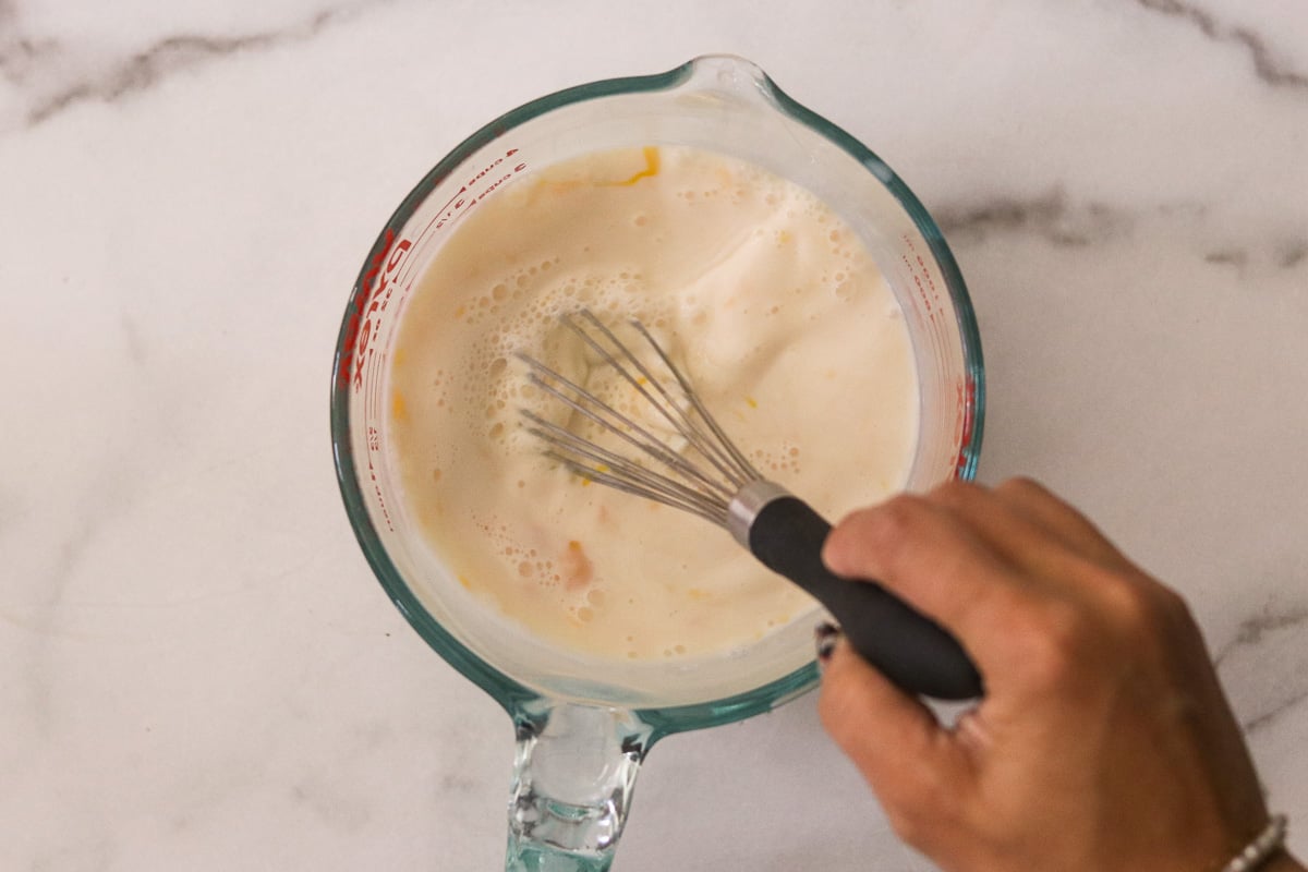 Milk, eggs, and vanilla being whisked in a glass measuring cup.