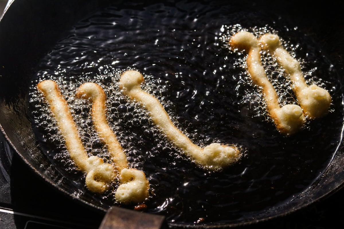 Frying funnel cake strips in hot oil until golden brown and crispy.