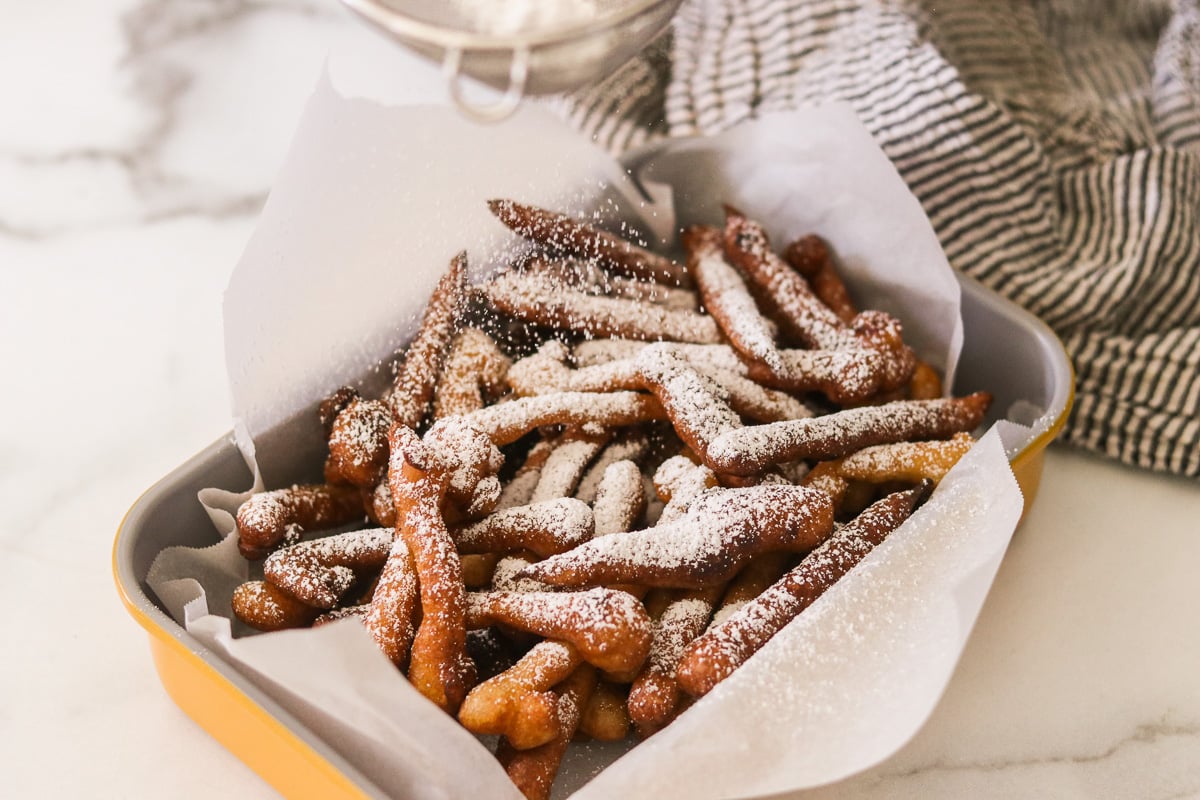 Funnel cake fries being dusted with powdered sugar before serving.