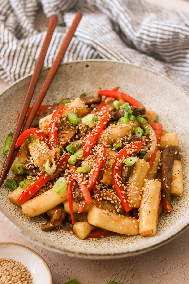 an up close shot of gungjung tteokbokki in a bowl with veggies, scallions, and sesame seeds