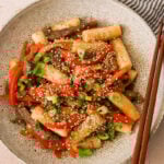 gungjung tteokbokki in a bowl with sauteed veggies topped with sesame seeds.