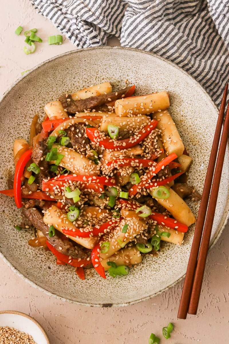 gungjung tteokbokki in a bowl with sauteed veggies topped with sesame seeds.