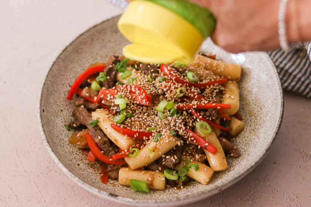 sprinkling sesame seeds atop a bowl of gungjung tteokbokki