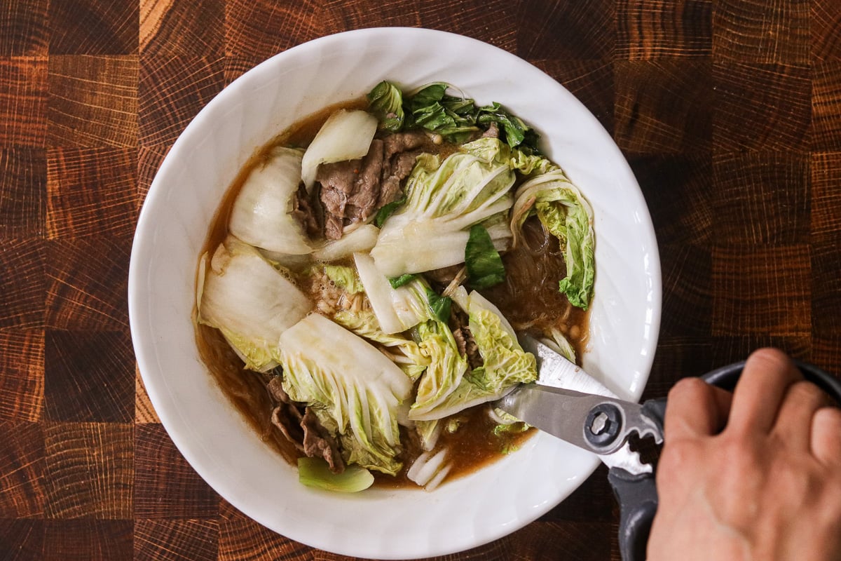 Cooked microwave hot pot being cut into bite-sized pieces with kitchen shears after heating.