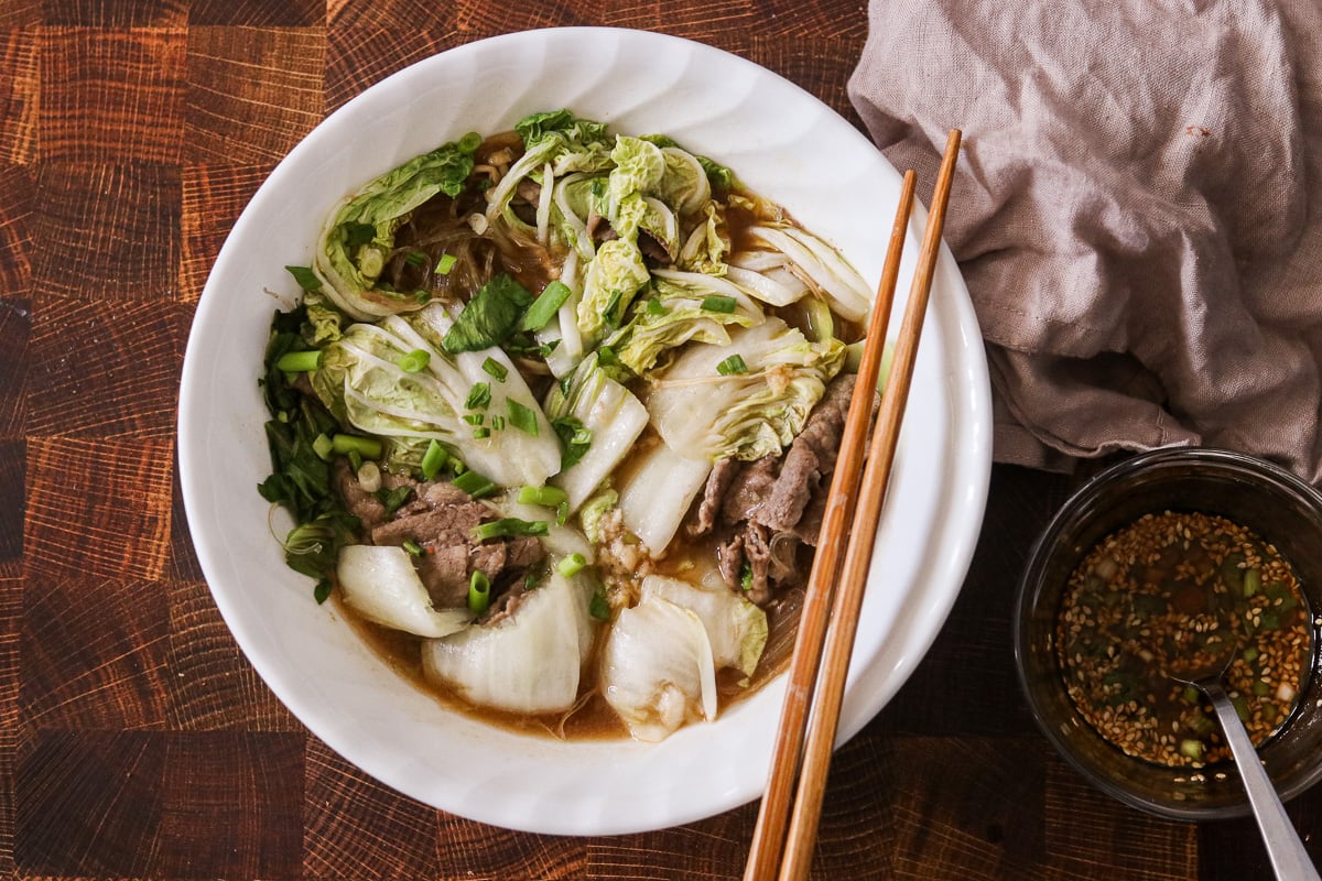 Microwave hot pot in a bowl with chopsticks on top and a small bowl of dipping sauce on the side.
