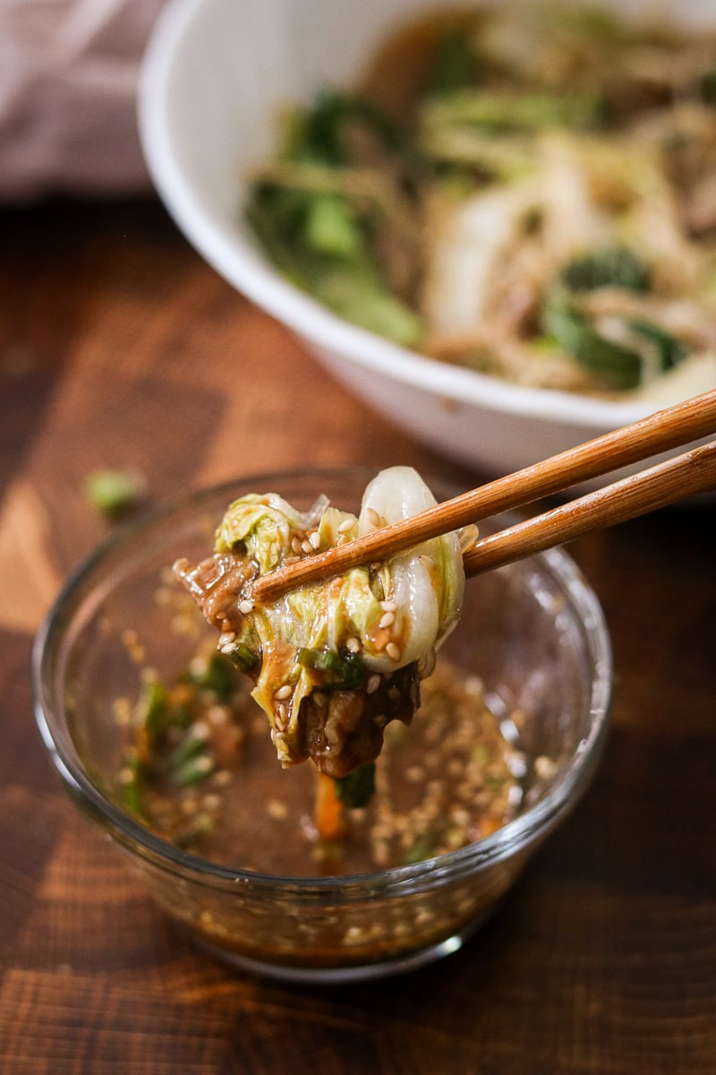 Close-up of microwave hot pot in a clear bowl with chopsticks picking up noodles and beef.