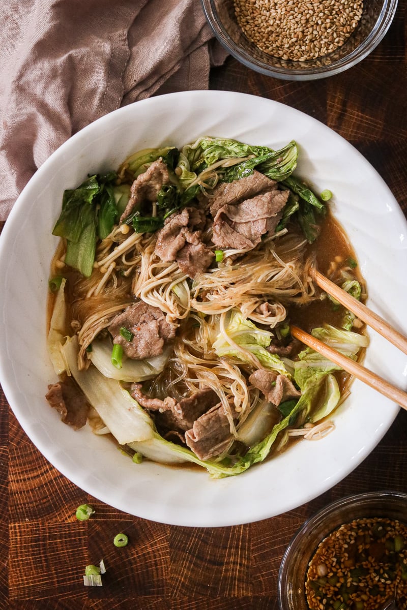 Microwave hot pot in a bowl with chopsticks, showing noodles, beef, and vegetables in broth.