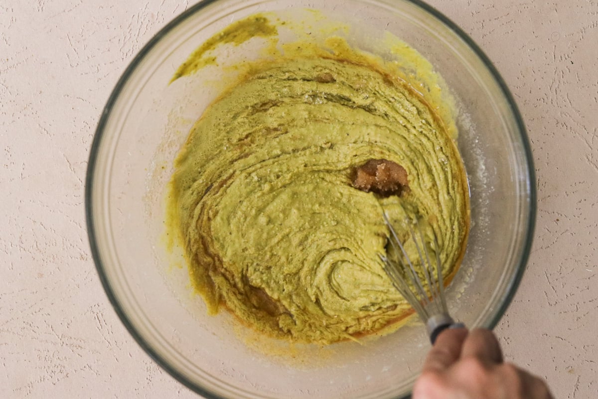 Sugar, sea salt, and vanilla extract being stirred into melted pistachio butter and white chocolate mixture.