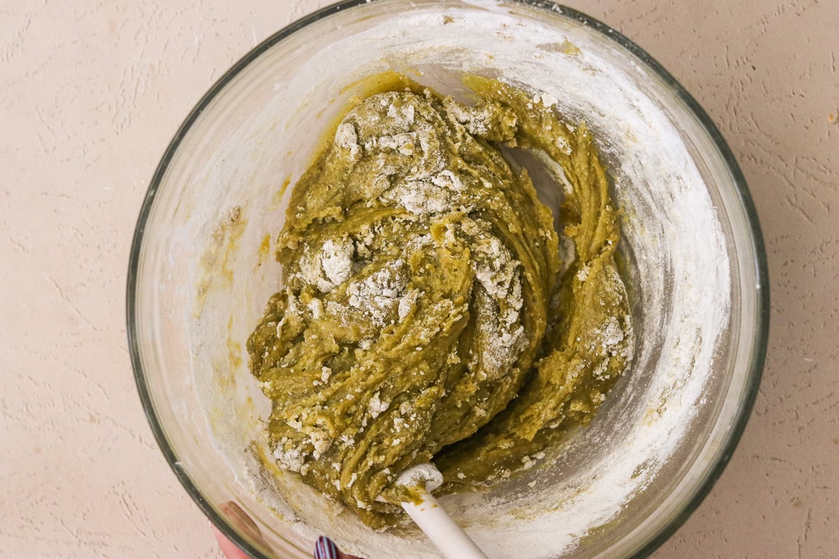 Gluten-free flour being folded into pistachio blondie batter in a mixing bowl.