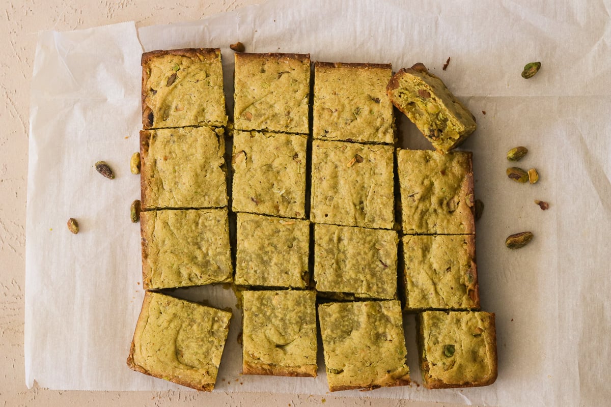 Freshly baked pistachio blondies sliced and cooling on parchment paper.