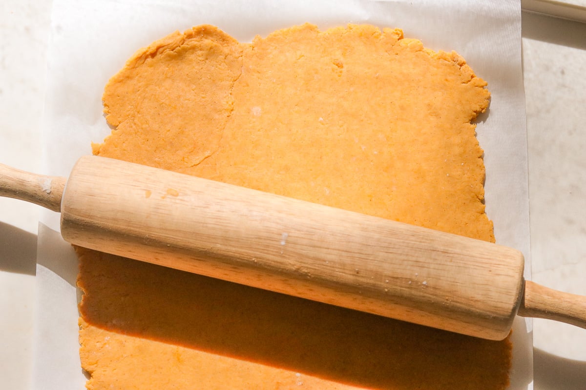 Rolling sweet potato cracker dough with a rolling pin on parchment paper to about 1/8 inch thickness.