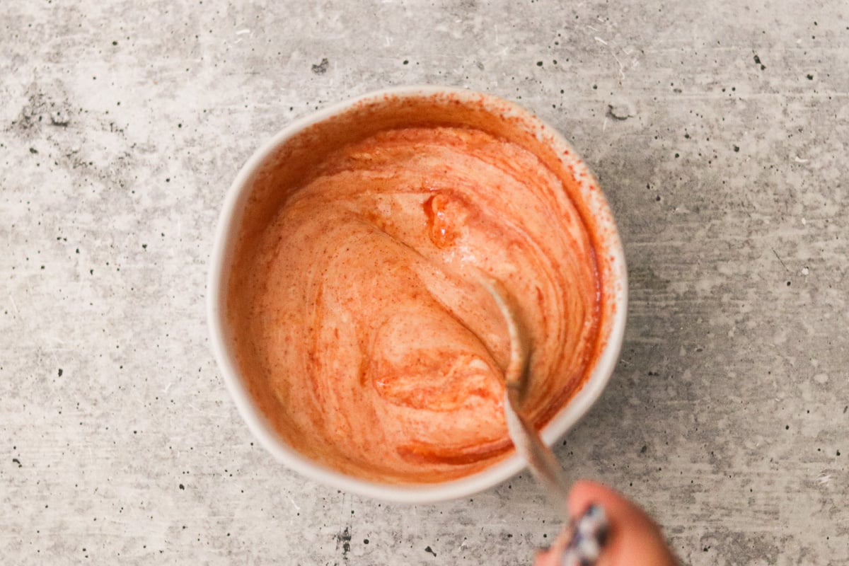 Mayo, ketchup, sugar, mirin, paprika, and garlic powder in a bowl being mixed with a spoon.
