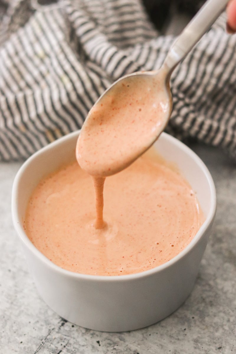 A small white bowl with homemade yum yum sauce; a spoon lifting some out.
