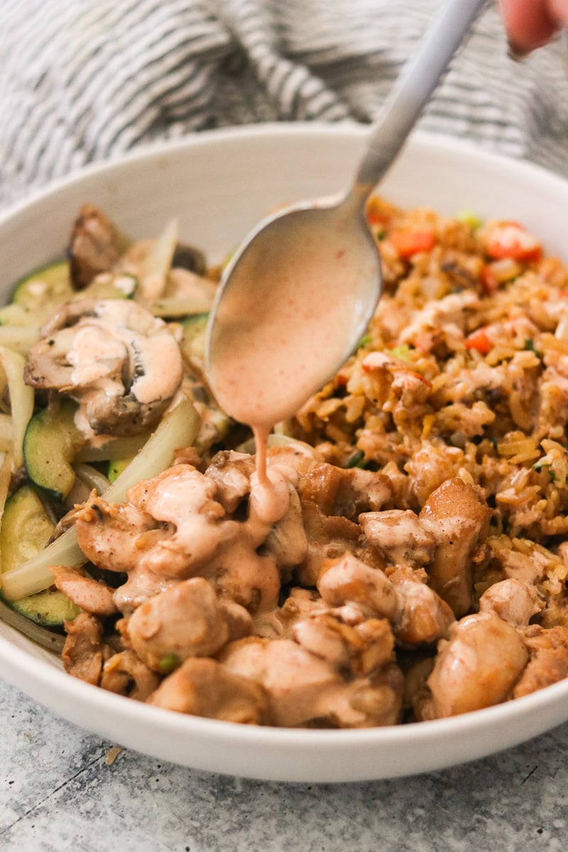 Homemade yum yum sauce being spooned over a hibachi bowl.