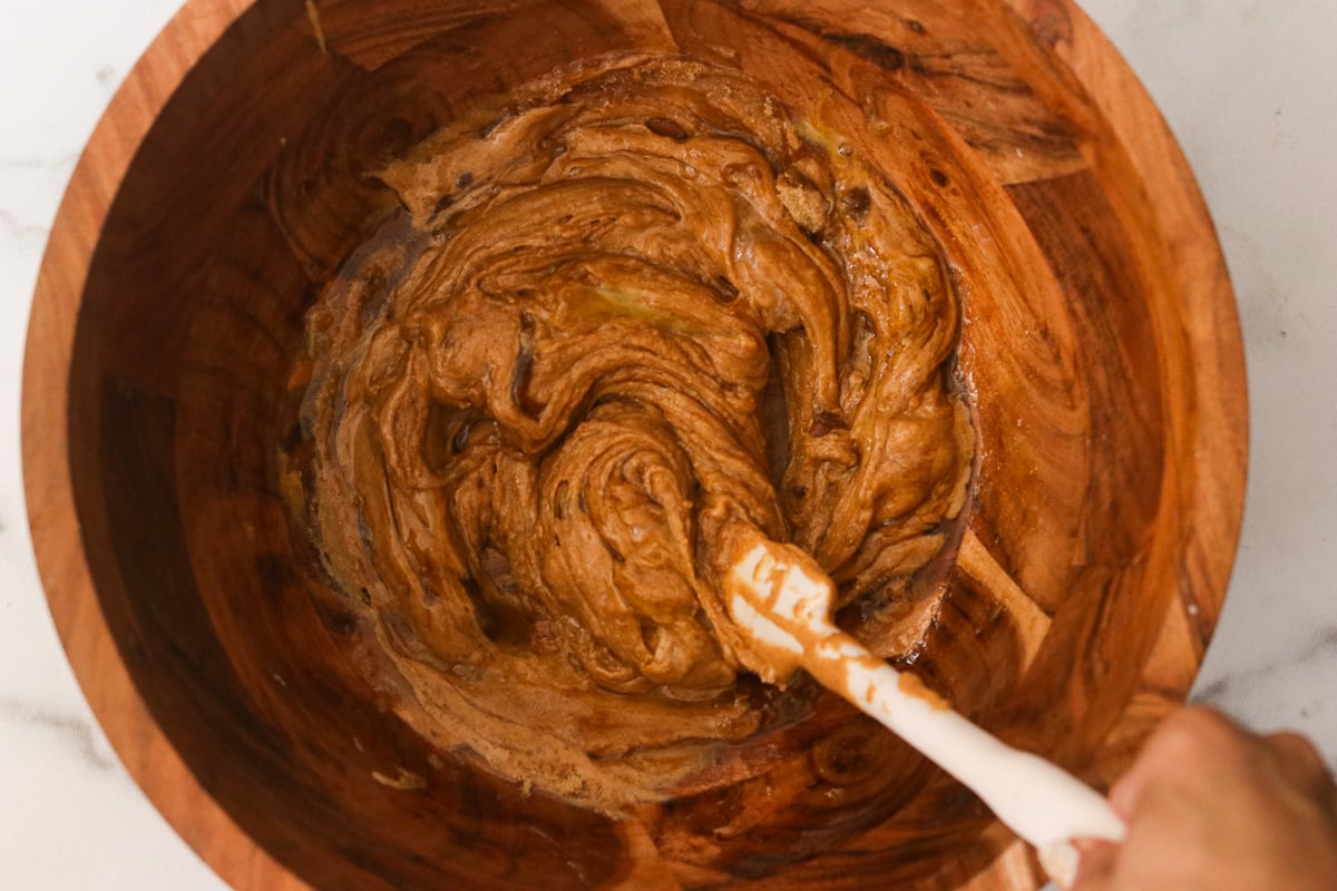 Mixing peanut butter cookie dough in a wooden bowl until smooth and fully combined.