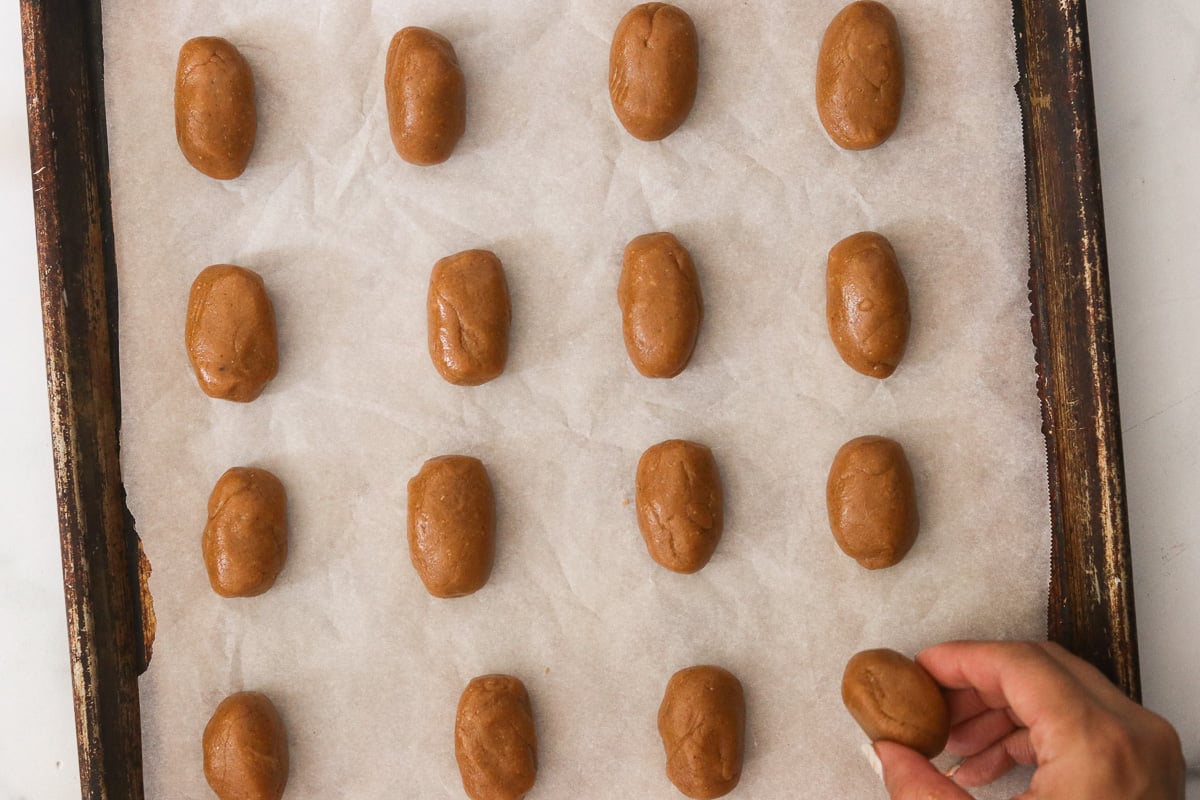 Rolling gluten-free nutter butter dough into logs and placing them on a parchment-lined baking sheet