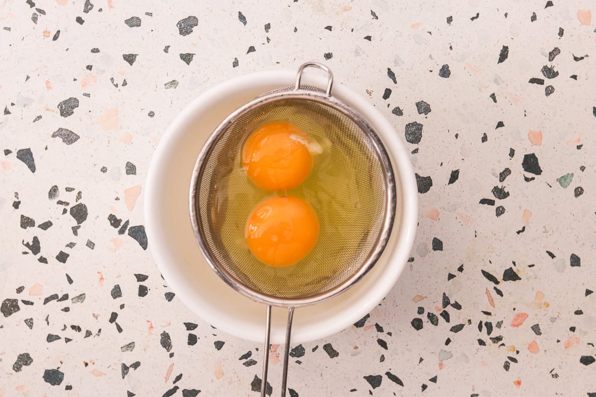 Eggs being strained through a fine mesh strainer to remove watery whites.