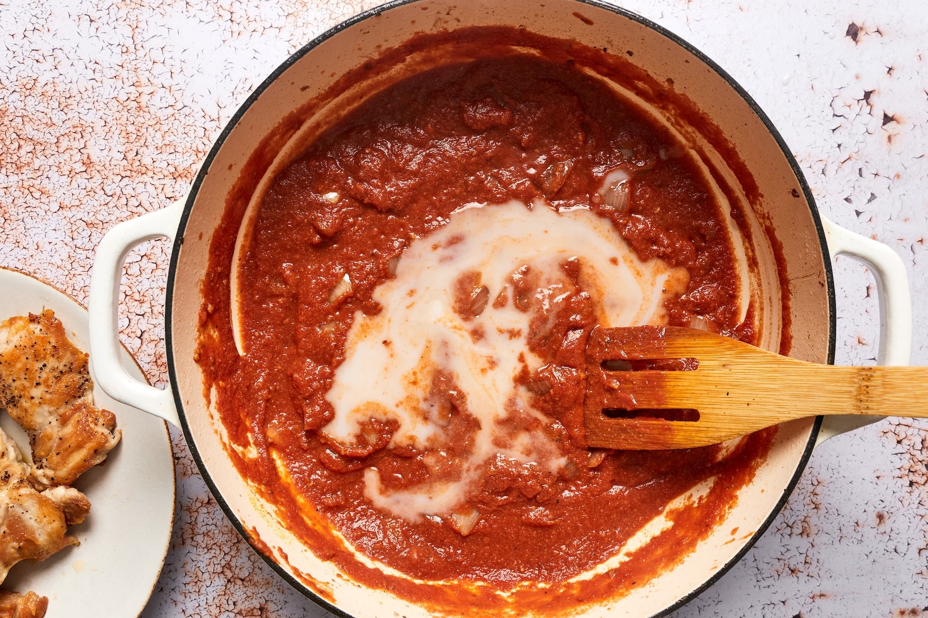 Coconut milk being stirred into the tomato sauce in a skillet.