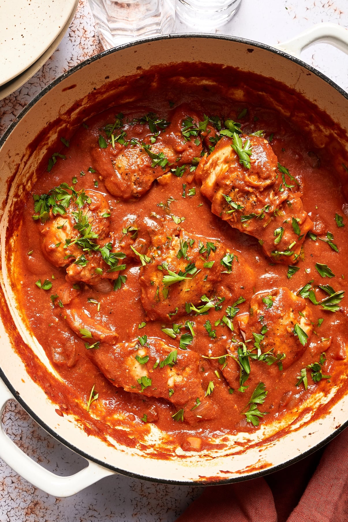 Creamy tomato chicken simmering in a large skillet with a creamy tomato sauce and fresh chopped basil on top.
