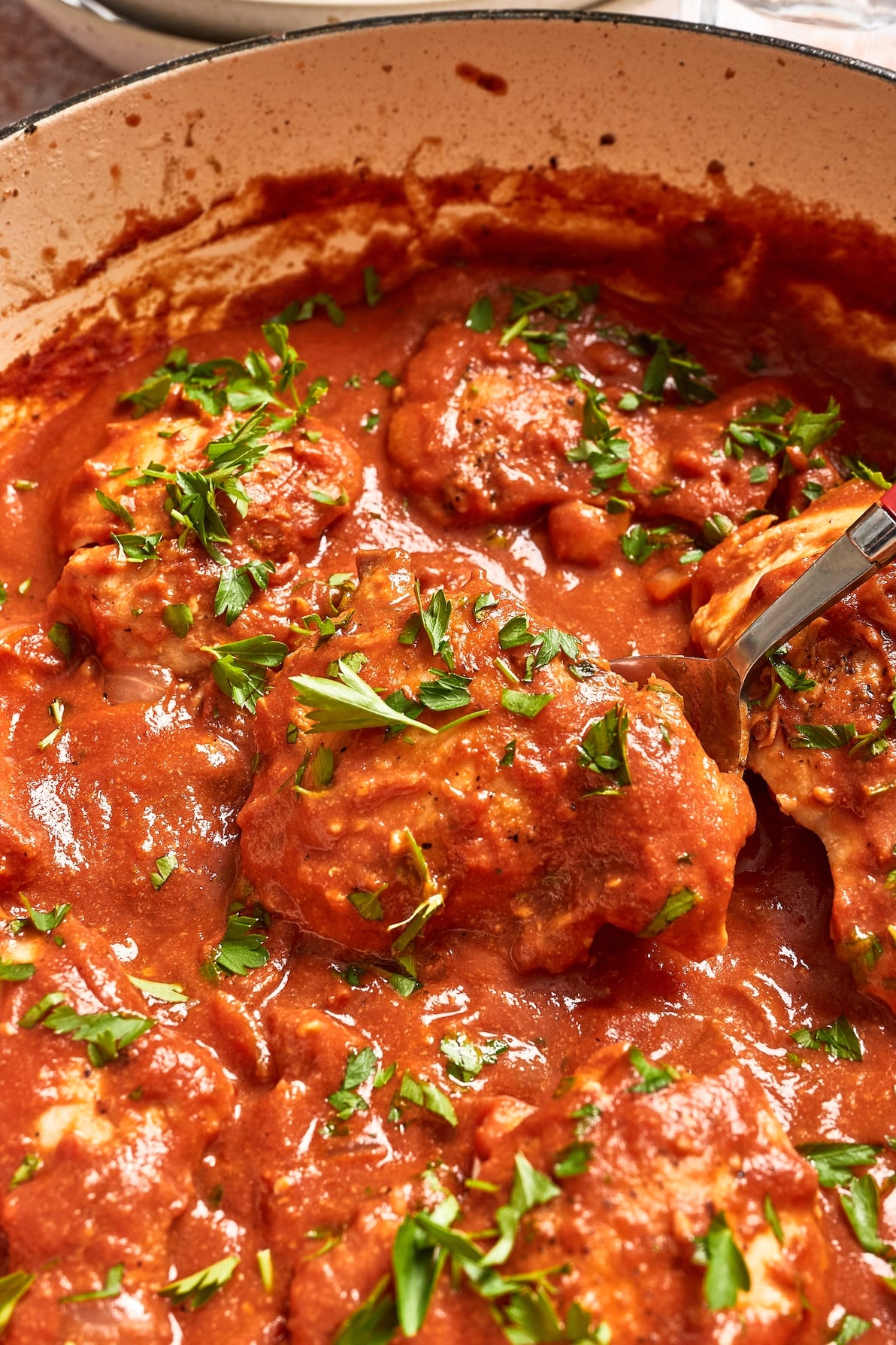 Close-up of creamy tomato chicken in a skillet with basil garnish while a spoon lifts a tender piece of chicken from the sauce.