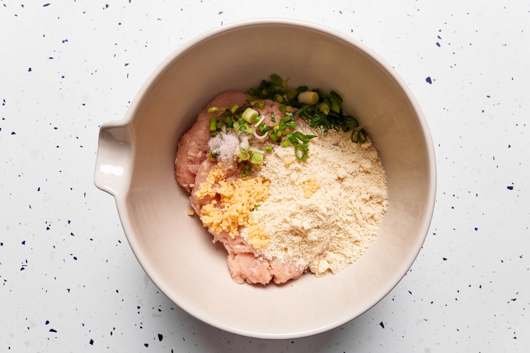 Ground chicken, almond meal, garlic, green onions, and seasonings combined in a large mixing bowl for buffalo chicken meatballs.