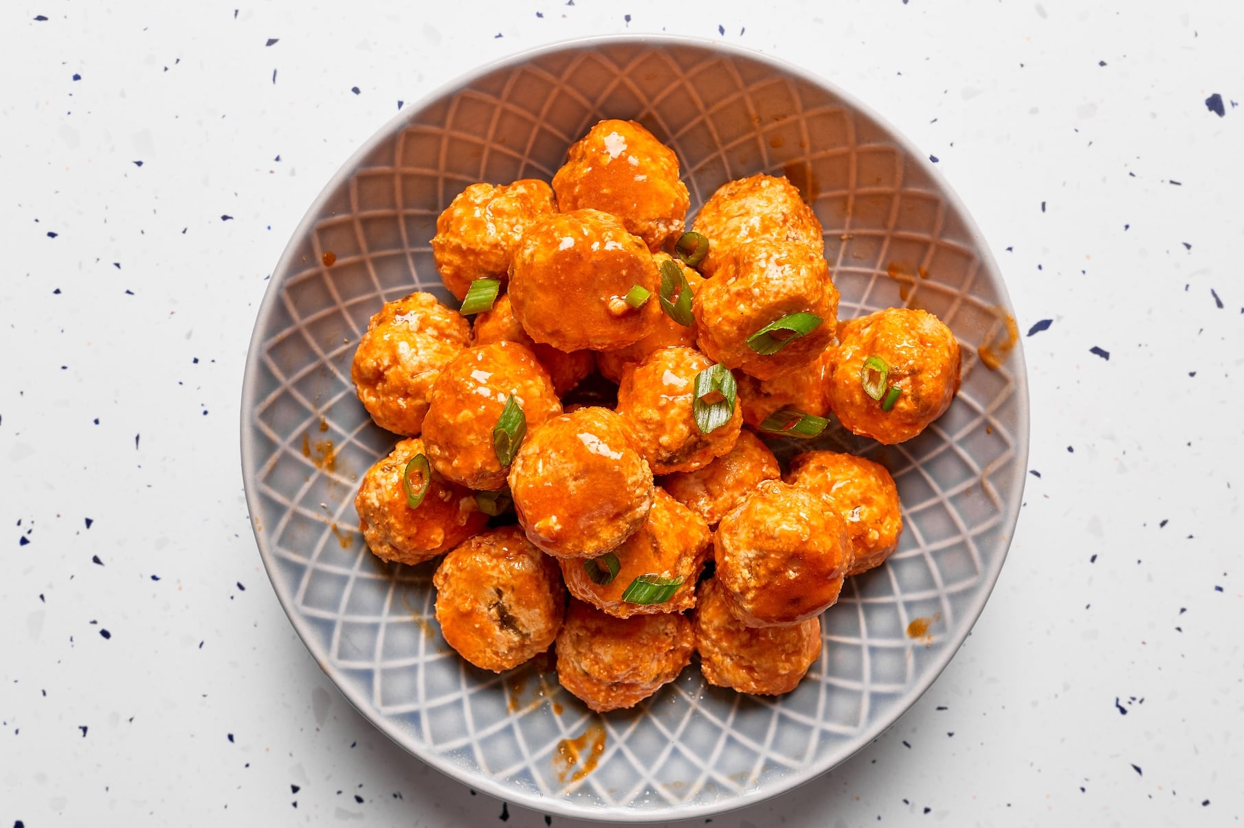 Buffalo chicken meatballs in a small serving bowl garnished with chopped green onions.