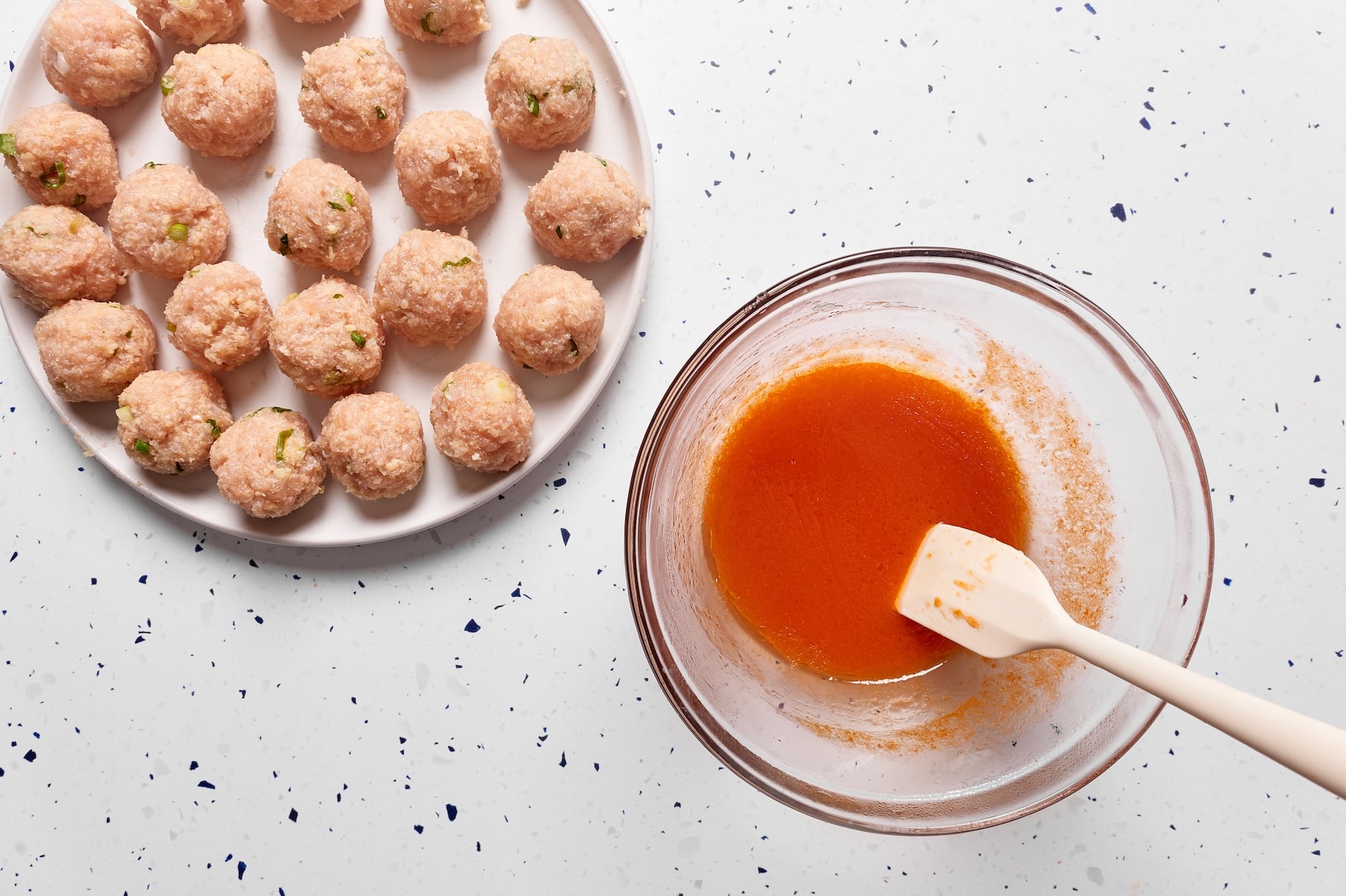 Homemade buffalo sauce in a glass bowl beside uncooked buffalo chicken meatballs ready for the Instant Pot.
