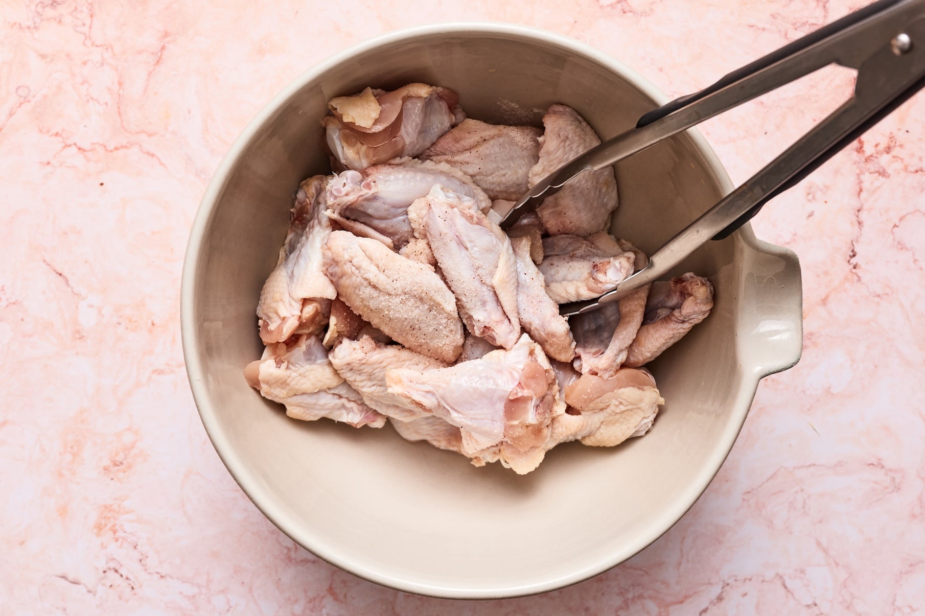Raw chicken wings in a mixing bowl sprinkled with salt and gently tossed to coat evenly.