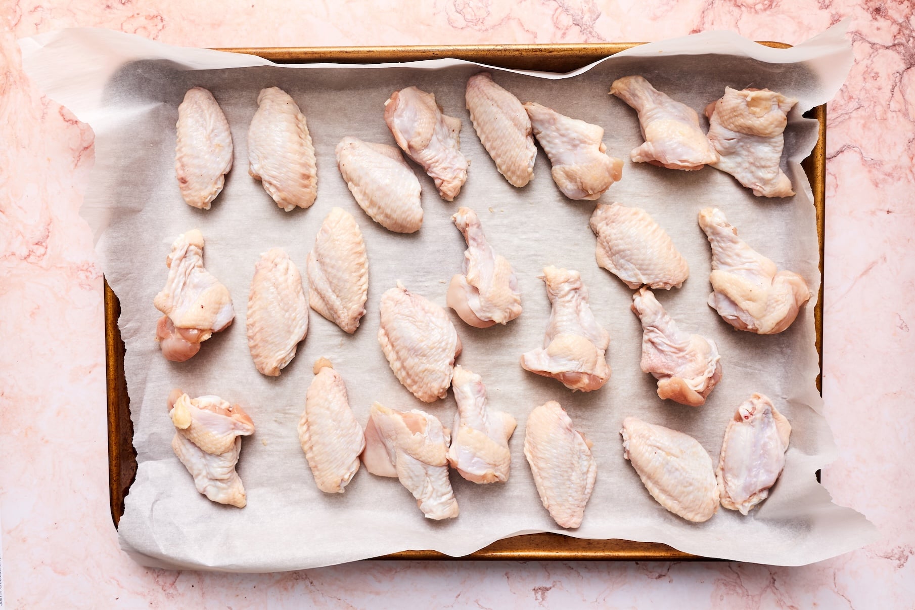 Raw chicken wings arranged on a parchment-lined baking sheet before baking.