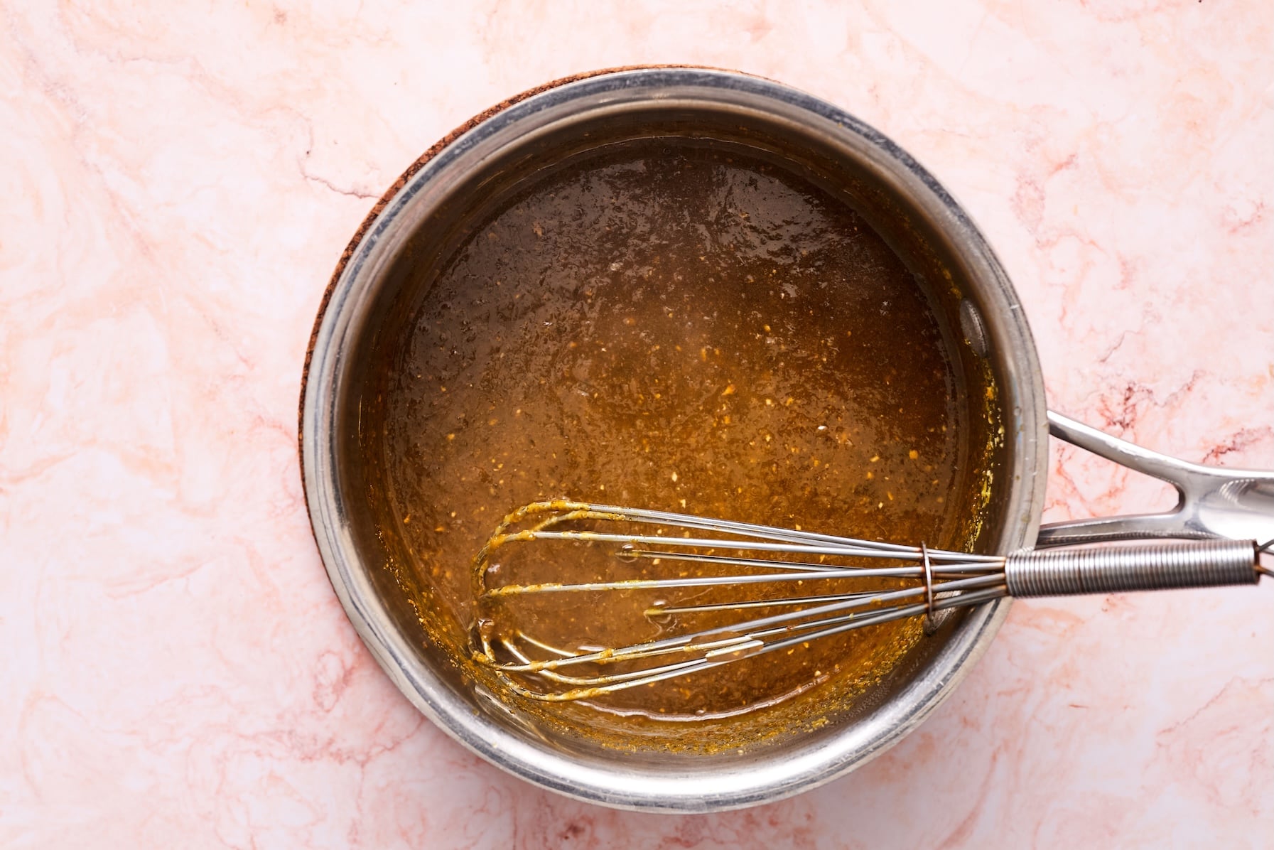 Paleo wing sauce heating in a saucepan over medium heat with a whisk in the pot.