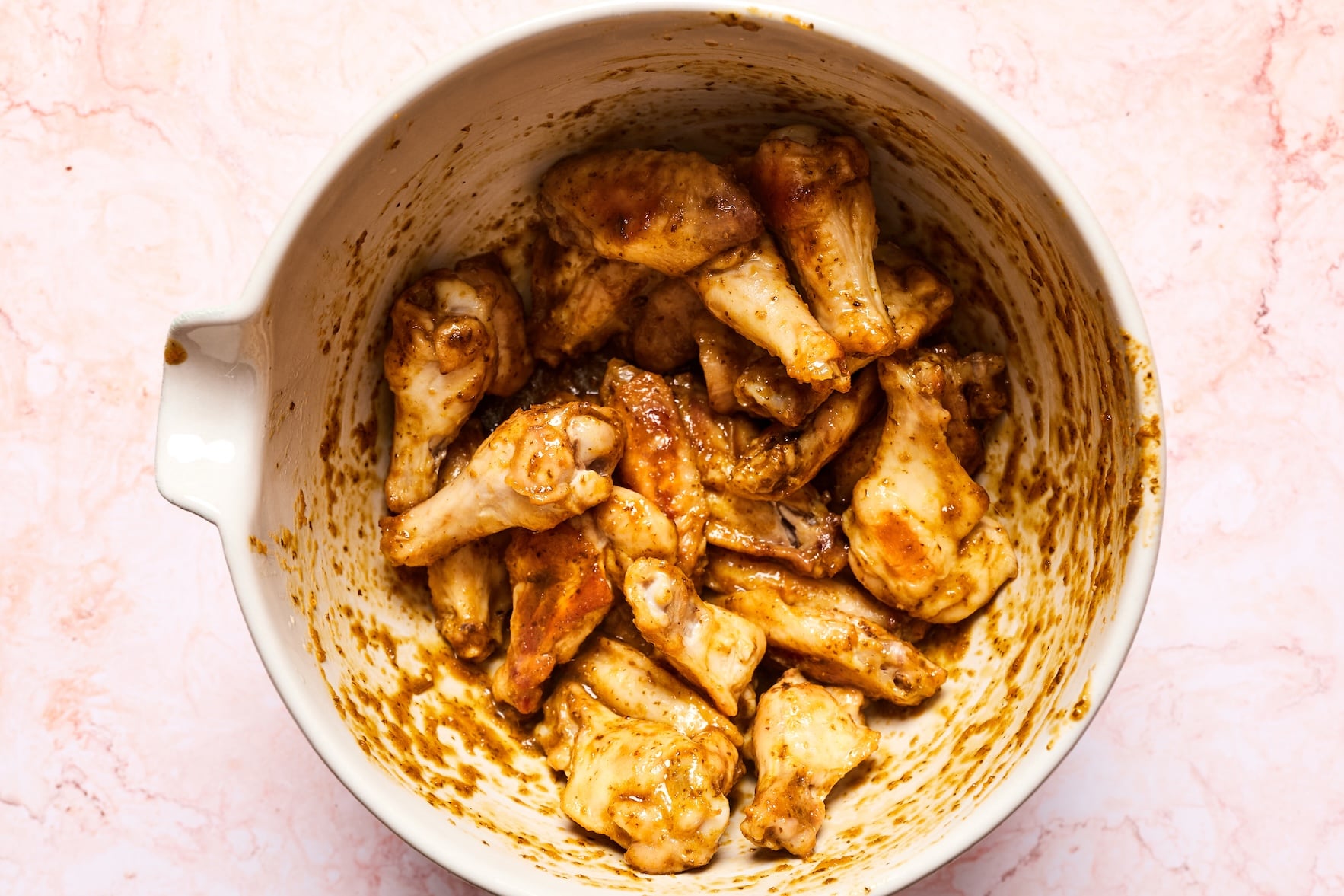 Cooked chicken wings tossed in sauce in a large mixing bowl until evenly coated.