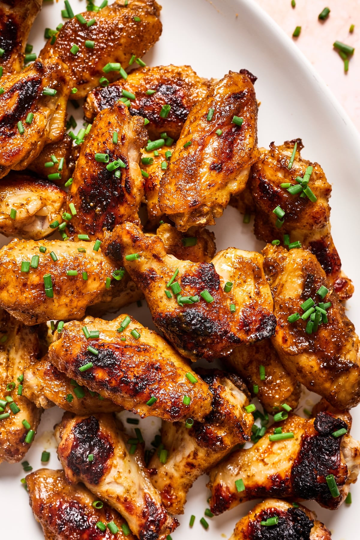 Close-up of crispy paleo chicken wings on a serving platter garnished with chopped chives.