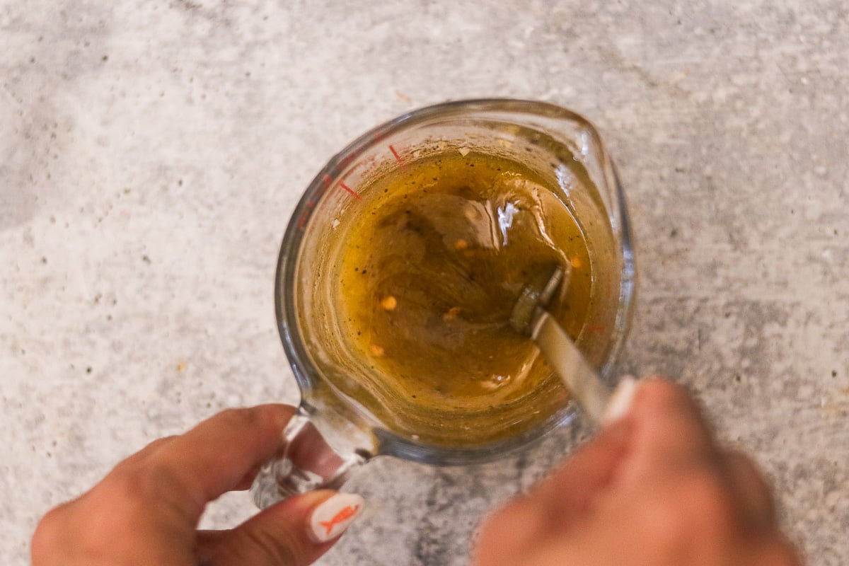 Lemon garlic dressing ingredients being mixed in a glass measuring cup.