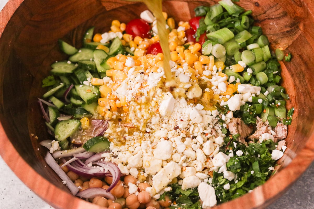 Lemon dressing being poured over chickpea tuna salad in a mixing bowl.
