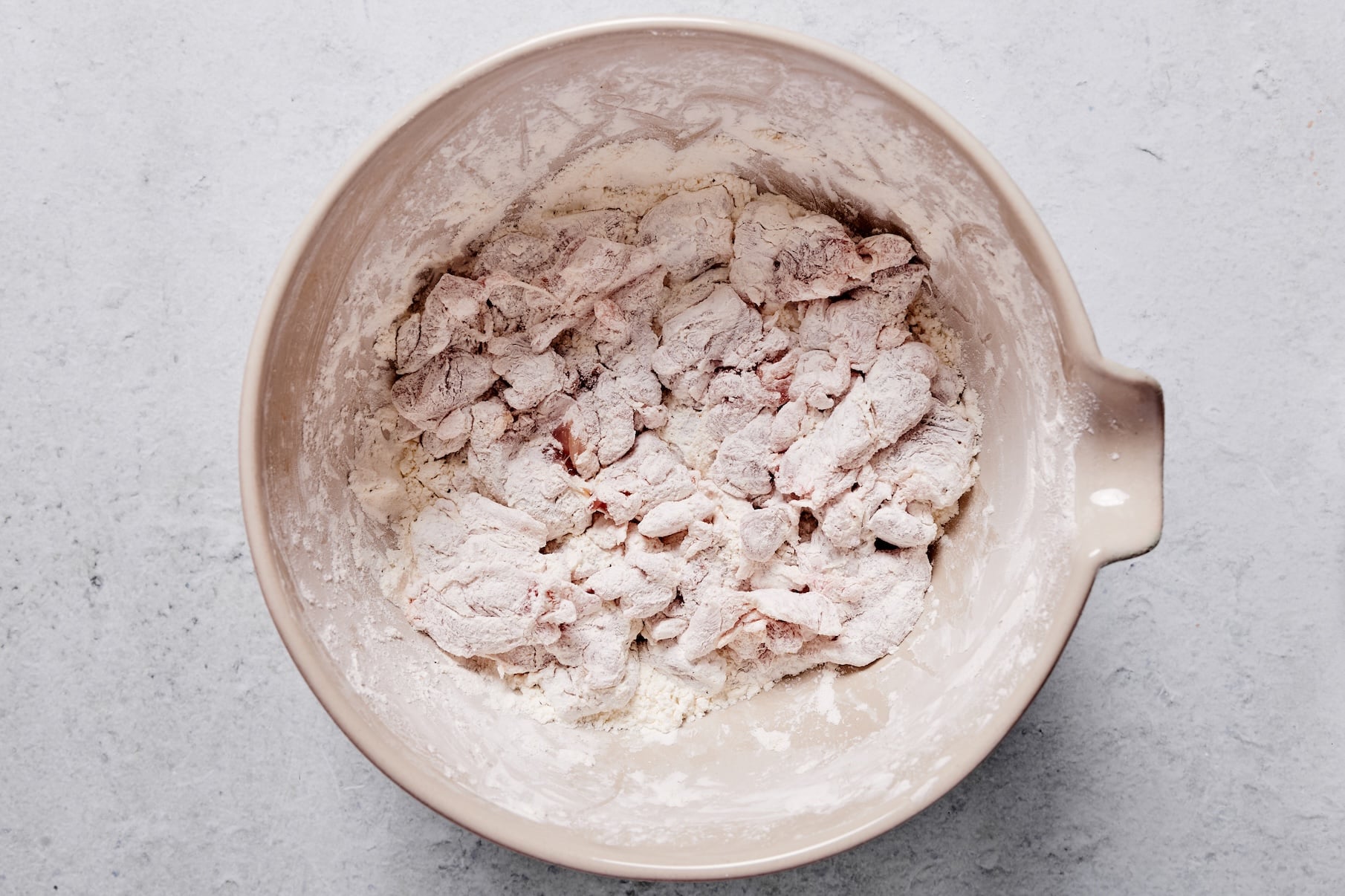 Chicken pieces tossed in a cornstarch, garlic powder, salt, and pepper coating in a large mixing bowl.