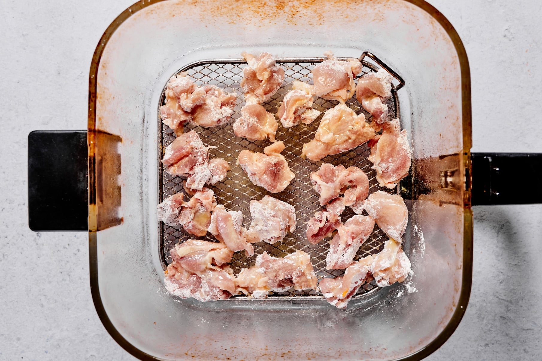 Coated chicken pieces arranged in a single layer in an air fryer basket.