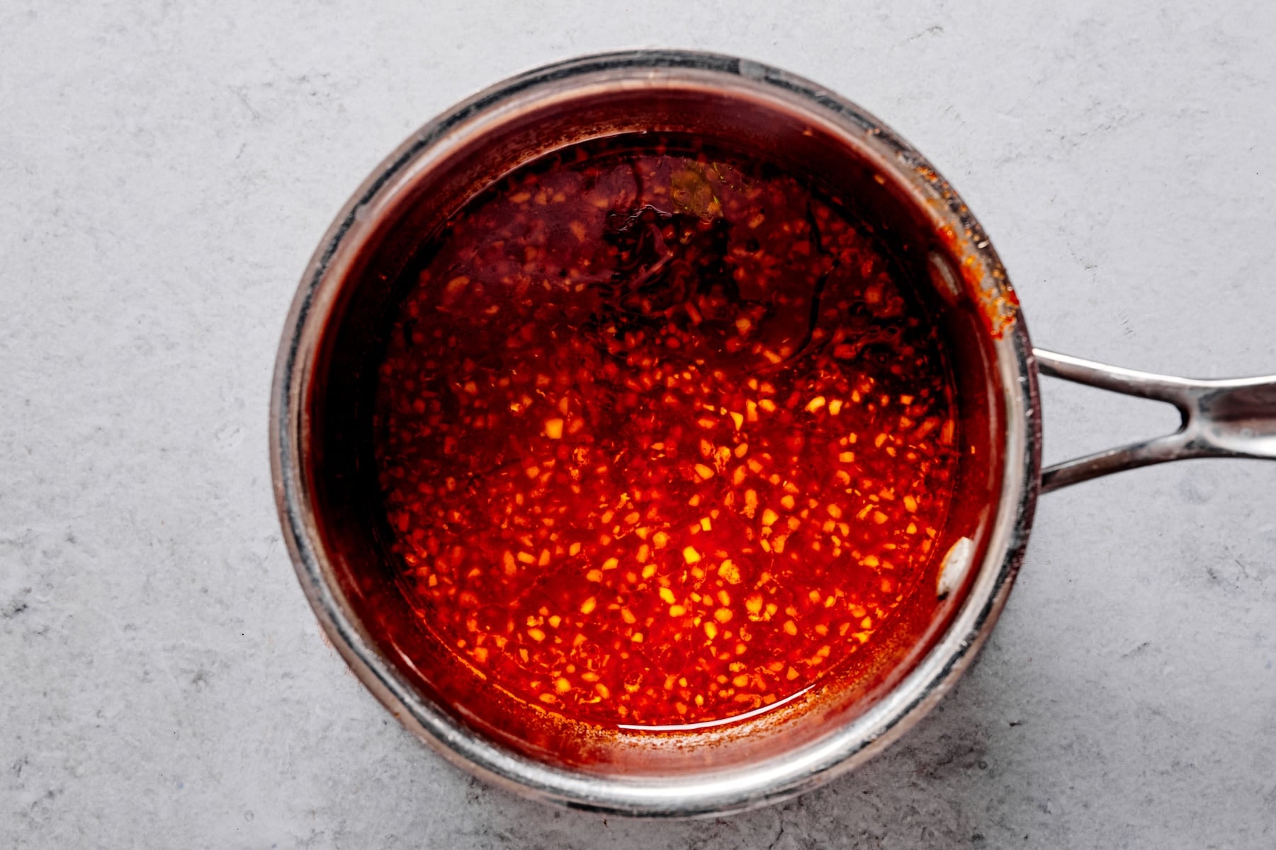 Gochujang sauce simmering in a saucepan with garlic and sesame oil until slightly thickened.