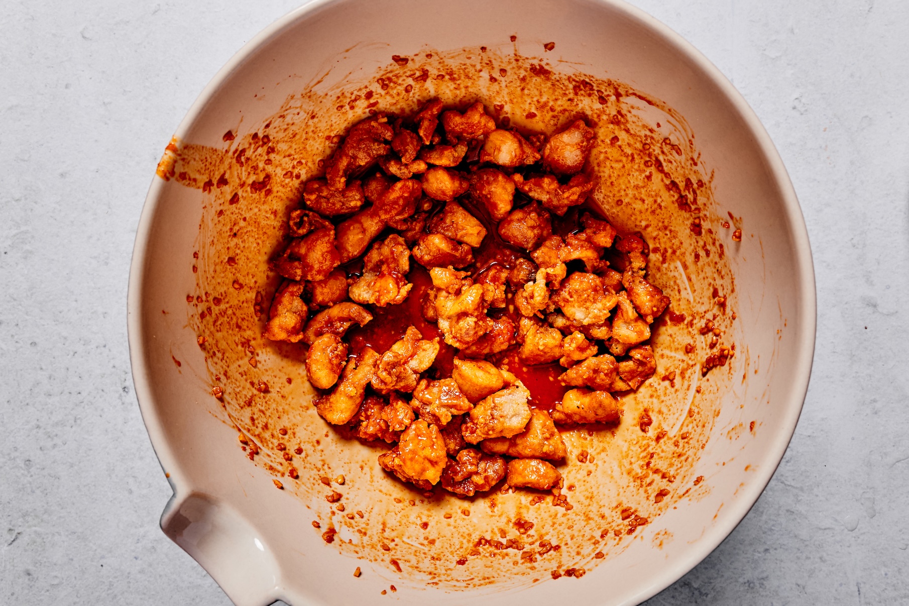 A bowl of cooked chicken tossed in sticky gochujang sauce until evenly coated.