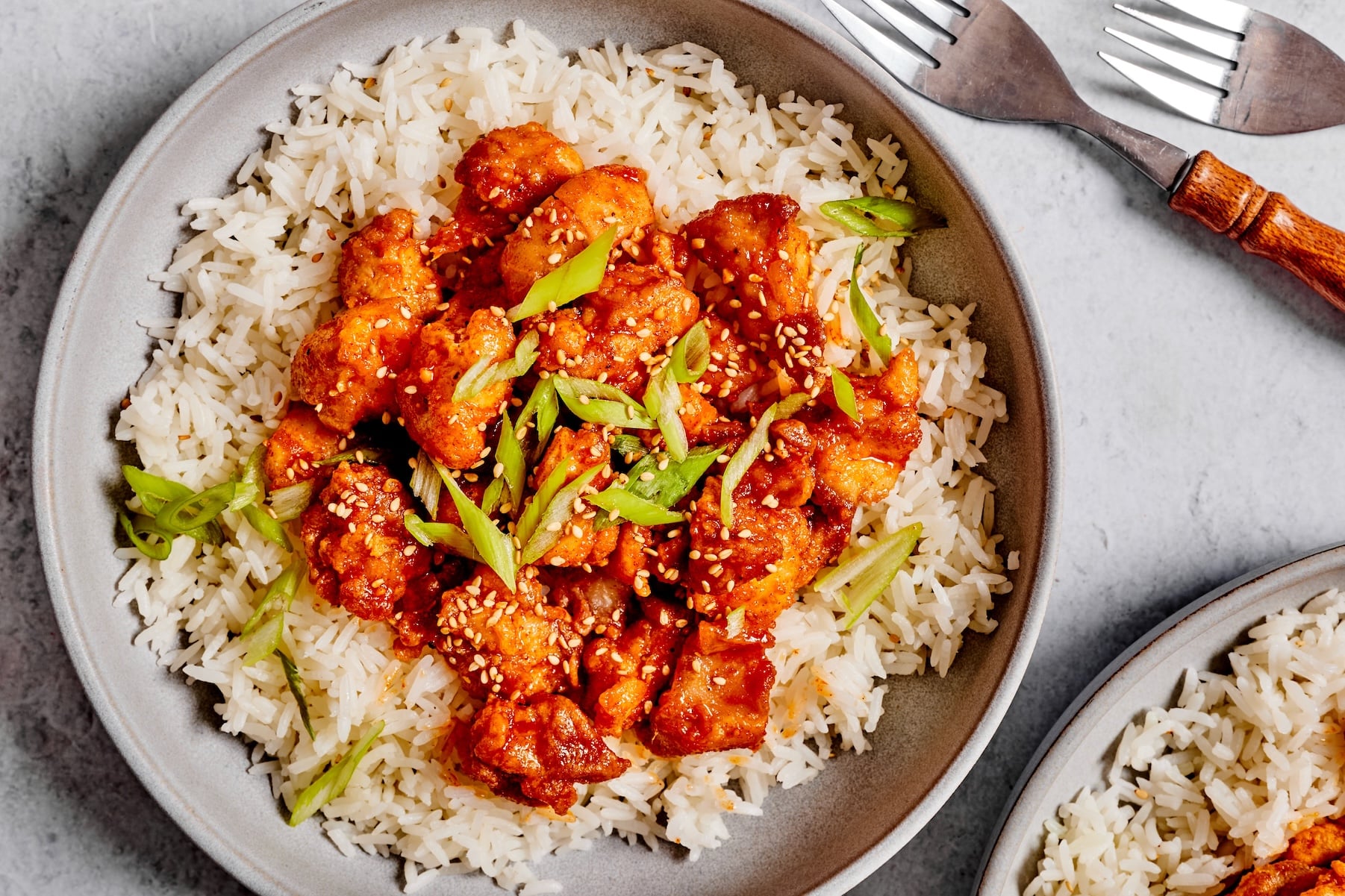 Gochujang chicken served over rice and garnished with sliced green onions and sesame seeds.