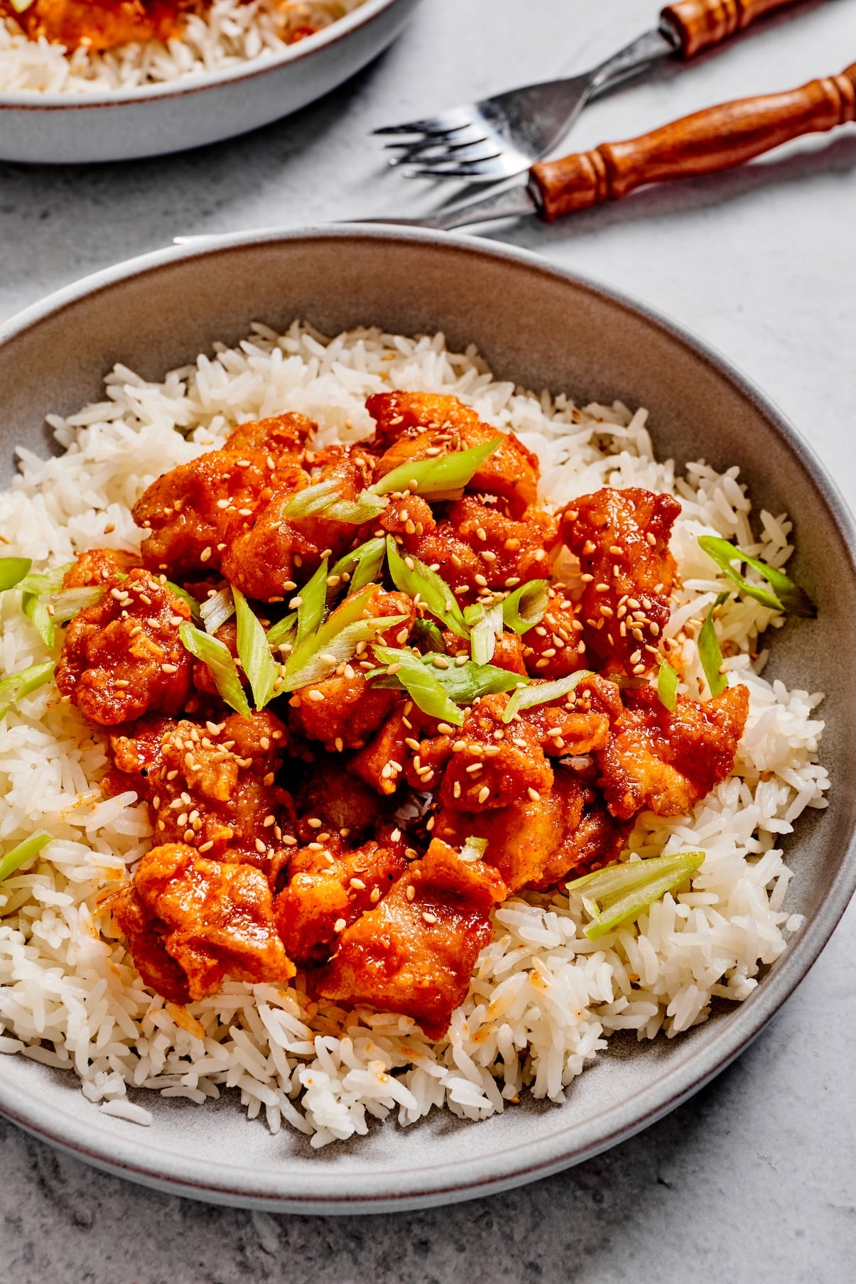Close-up of sticky gochujang chicken over rice with green onions and sesame seeds.