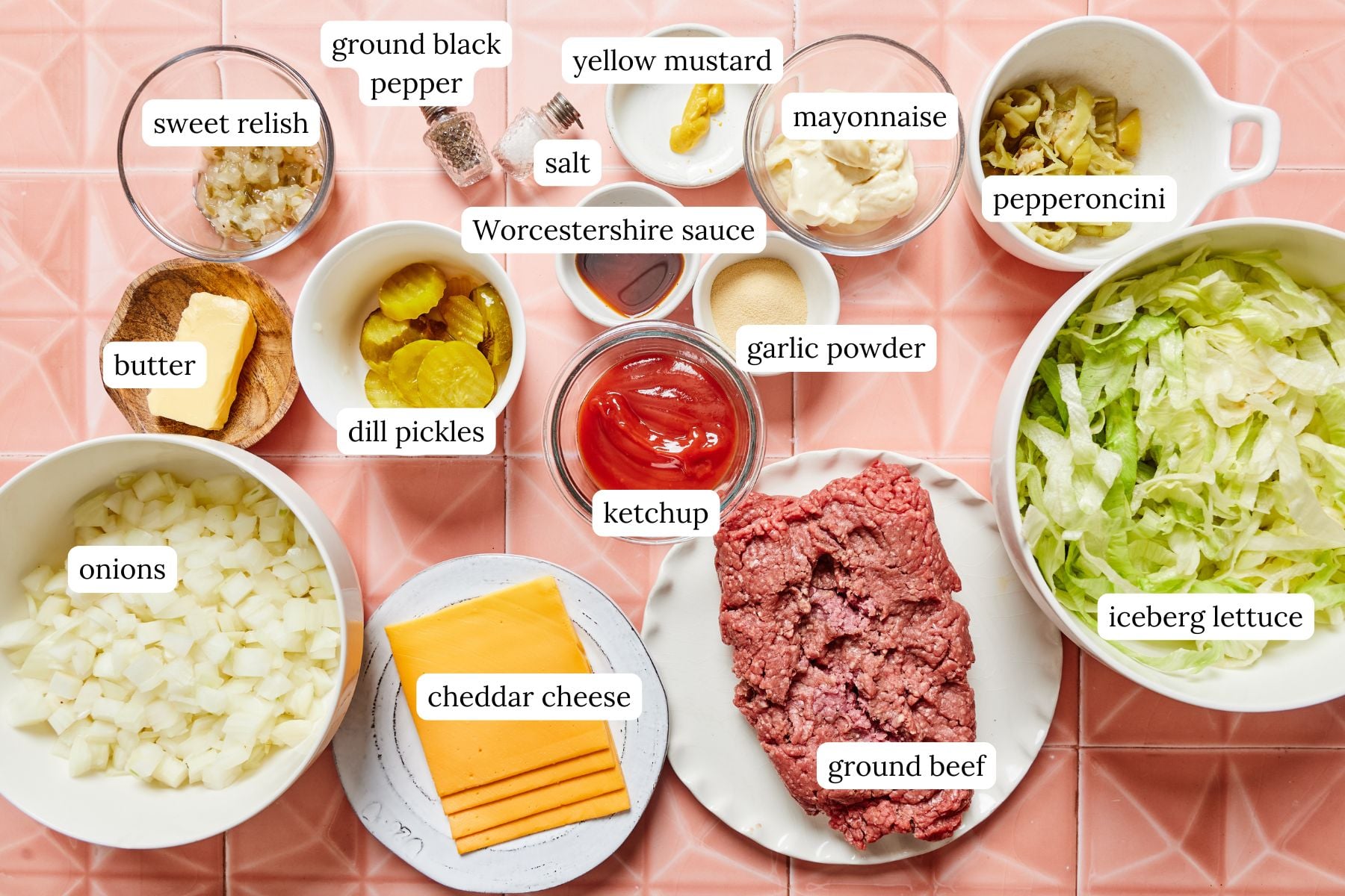 Cheeseburger salad recipe ingredients labeled and laid out on a light pink countertop.