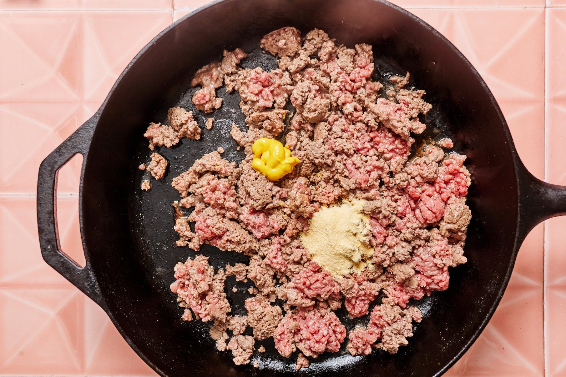 Ground beef cooking in a skillet with Worcestershire sauce, yellow mustard, garlic powder, salt, and pepper.
